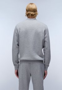 Sudadera gris hecha de una mezcla de algodón, con cuello redondo, puños y dobladillo acanalados, y una textura suave. Llevada con pantalones grises a juego.