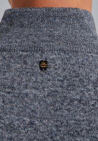 Knitted sweater in a heathered dark blue fabric. Features a high collar and a black label with gold text on the back.
