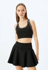 Sort cropped tanktop med hvid kant, parret med en flared sort nederdel. Materialet ser glat og strækbart ud, hvilket giver et tætsiddende look.