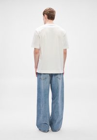 Tricou alb din bumbac cu mâneci scurte, combinat cu blugi oversized de denim albastru deschis, cu buzunare în spate și croială lejeră.