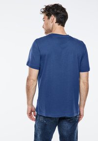 T-shirt di cotone blu con maniche corte, scollatura rotonda e vestibilità comoda, abbinata a jeans di denim blu. Design semplice, senza motivi visibili.