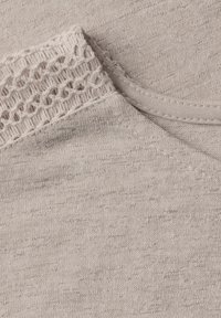 Světle šedá pletenina s texturovaným, krajkovým vzorem v oblasti dekoltu. Hladká struktura a jemné variace barev.