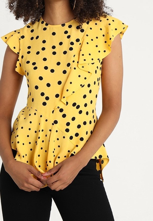 Žlutý top s černými puntíky, volánkovými rukávy a peplum střihem. Obsahuje knoflíkové detaily na boku a strukturovanou tkaninu.