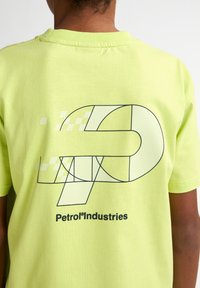 Neon žluté bavlněné tričko s grafikou v černé barvě, která obrysově znázorňuje geometrické tvary a text "Petrol Industries" na spodní straně.