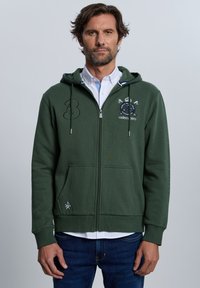 Sudadera con capucha verde con cremallera, hecha de mezcla de algodón, con un bolsillo frontal, detalles bordados y un cuello interior blanco a contraste.
