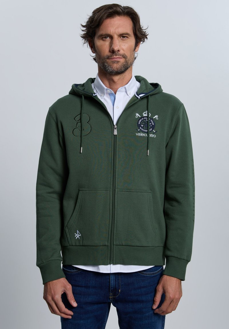 Sudadera con capucha verde con cremallera, hecha de mezcla de algodón, con un bolsillo frontal, detalles bordados y un cuello interior blanco a contraste.