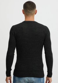 Dark gray, long-sleeve sweater with a textured ribbed design. Fitted shape, round neck, and ribbed cuffs at the wrists. Worn backwards.
