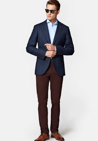 Granatowa marynarka w kratę, jasnobłękitna koszula, brązowe spodnie i brązowe buty. Marynarka ma strukturalny krój z klapami i guzikami na mankietach.