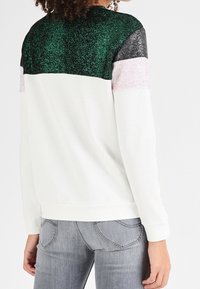 Sudadera blanca con un diseño de bloques de color texturizado en verde, negro y rosa brillante en la parte posterior, con un corte relajado y mangas largas.