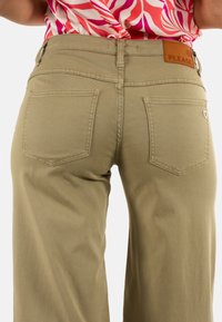 Pantalones de pierna ancha en color beige con una textura suave, que cuentan con dos bolsillos traseros y una etiqueta de cuero en la cintura, marcada con "POR FAVOR".