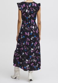 Abito maxi floreale con maniche a volant, base nera, fiori bianchi, rosa e blu, design a strati, abbinato a stivali bianchi alla caviglia.