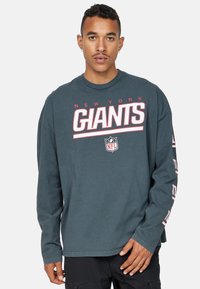 Pitkähihainen crewneck-t-paita tummansinisellä pohjalla, jossa on "New York Giants" -grafiikkaa valkoisena ja punaisena edessä ja hihassa; puuvillamateriaali.