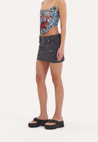 Kleurige, patroon tanktop met spaghettibandjes, gecombineerd met een grijze denimrok met riemlussen en voorzakken. Zwarte platform sandalen.