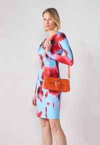 Robe colorée en bleu avec des motifs rouges et roses, fabriquée en matériau extensible ; accompagnée d'un petit sac à main orange avec une fermeture en or.