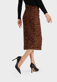 Gonna a tubino con stampa leopardata marrone dal design elegante, abbinata a scarpe con tacco appuntito nere. Tessuto liscio e silhouette aderente.