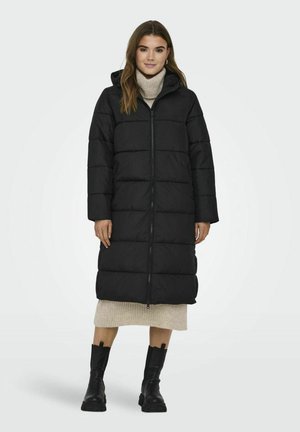 Long black puffer coat with a hood, featuring a front zipper and horizontal quilted design, paired with a cream turtleneck and black boots.