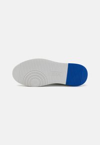 Sole of a sneaker featuring a textured white rubber base with a blue accent at the heel and circular pattern near the center.