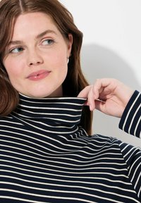 Marinblå och krämrandig polotröja med ribbad struktur. Kragen är vikt, och tyget verkar mjukt och elastiskt.