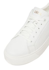 Weißer Ledersneaker mit strukturierter Oberfläche, flachen Schnürsenkeln und einem goldenen Logo. Verfügt über eine Gummisohle mit geriffeltem Muster für besseren Halt.