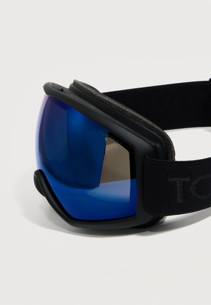 Lunettes de ski noires avec lentille incurvée réfléchissante bleue et sangle noire réglable sur fond blanc.