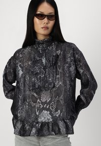 Blusa a stampa serpente nera e grigia con colletto arricciato e dettagli frontali, chiusura con bottoni e orlo arricciato. Tessuto leggero.