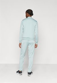 Jasnoniebieski sportowy dres wykonany z poliestru, składający się z kurtki na zamek oraz zwężanych spodni, o gładkiej fakturze i ściągaczach przy mankietach.