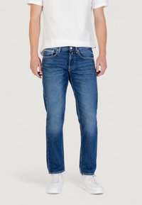 Jeans in denim azzurro chiaro con vestibilità dritta, design a cinque tasche e leggere sfumature. Abbinati a una t-shirt bianca e sneakers bianche.