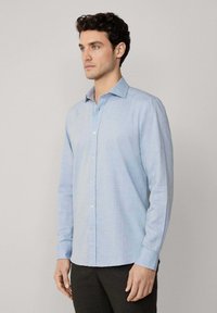 Camicia a maniche lunghe di colore azzurro chiaro, con colletto, realizzata in tessuto morbido. Presenta un design a vestibilità slim. Nessun motivo o dettaglio visibile.
