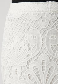 Tissu blanc brodé présentant un motif de dentelle détaillé avec des motifs floraux et une surface texturée, adapté pour des vêtements.