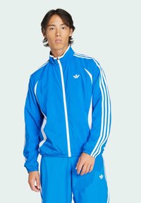 Blue athletic jacket with white stripes, high collar, zip closure, and logo on chest; made from smooth, lightweight material.