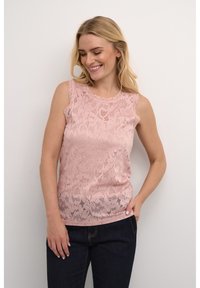 Rozā mežģīņu bezmugurkaula tops ar viļņotu dekoltē un sarežģītiem ziedu rakstiem, apģērbts virs tumšām džinsa biksēm.