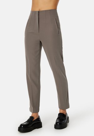 Pantaloni grigi chiari con vita alta, caratterizzati da pince, tasche laterali e una vestibilità sartoriale, abbinati a mocassini neri con plateau.