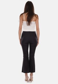 Pantaloni neri a campana realizzati in tessuto liscio, con una vestibilità elegante e due tasche posteriori; abbinati a un top fitted bianco.