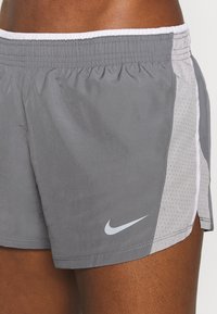 Pantalones cortos deportivos grises con un panel lateral de malla, cintura elástica y acentos blancos. Presenta un pequeño logo de Nike en gris en la parte frontal.