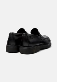 Pair of black leather slip-on loafers with thick rubber soles shown from the back on a plain white background.