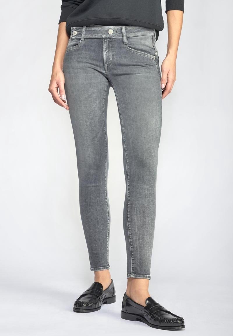 Osoba v přizpůsobených šedých džínách a černých kožených mokasínech, stojící na jednobarevném světlejším pozadí.