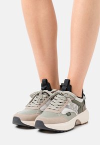 Baskets légères en nuances de vert olive et beige, présentant un mélange de suède et de mesh, avec des lacets ronds et un marquage audacieux sur le côté.