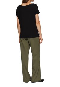 Black short-sleeve top with a scoop neckline paired with loose-fitting olive green pants, featuring a smooth texture and relaxed silhouette.