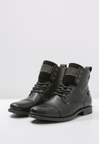 Stivaletti neri in pelle con inserti in camoscio, punta rotonda, design con lacci e hardware decorativo. Superiori testurizzati e tacco basso a blocco.