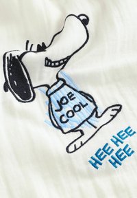 Biały materiał z haftowanym charakterem Snoopy w niebieskiej koszuli z napisem "JOE COOL". Dodatkowy tekst "HEE HEE HEE" w kolorze niebieskim.
