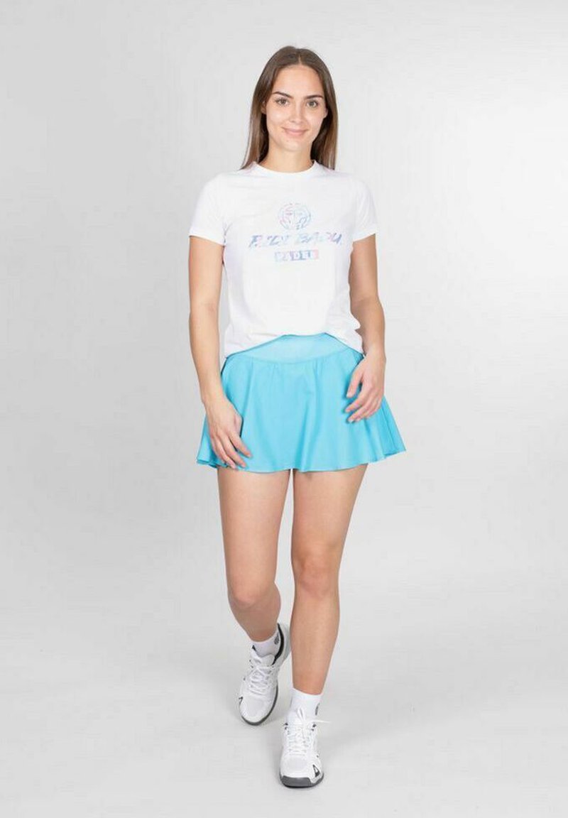 Jupe courte évasée bleue avec une texture lisse, assortie à un t-shirt blanc avec un imprimé coloré, et des chaussures de sport blanches.