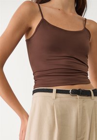 Bruine aansluitende camisole met dunne bandjes, gecombineerd met beige geplooide broek en een zwarte gevlochten riem. Gladde stof en zachte textuur.
