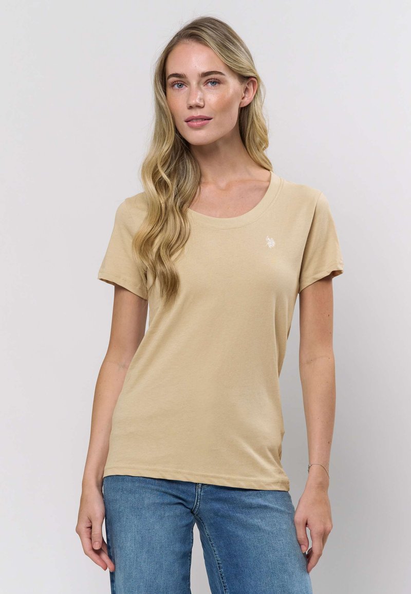 Béžové tričko s krátkým rukávem z měkké bavlny, s kulatým výstřihem a malým logem na levé hrudi.
