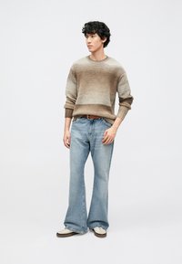 Brun och beige stickad tröja med gradient, lös passform, kombinerad med ljusblå utsvängda jeans och vita sneakers. Enkel bältesdetalj.