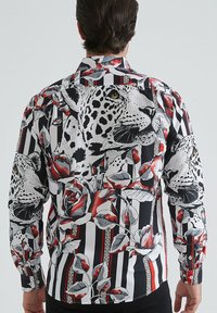 Chemise à col avec un motifrayé noir et blanc, ornée d'un grand imprimé léopard et floral dans des tons rouges et gris, avec des poignets à boutons.