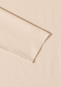 Tissu beige à manches longues avec une texture lisse et une légère élasticité. Présente un ourlet soigneusement cousu et un poignet plié.