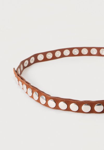 Ceinture en daim marron avec des clous ronds argentés régulièrement espacés sur toute sa longueur, disposée en cercle sur un fond uni et clair.