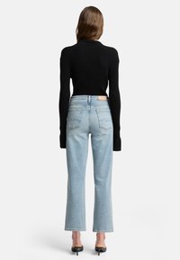 Maglione a costine nero abbinato a jeans a gamba larga di un blu chiaro, con due tasche posteriori e un'etichetta del marchio beige sulla vita. Tacchi neri.