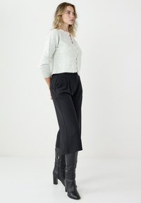 Jasnoszary krótki kardigan z guzikami, zestawiony z czarnymi spodniami z wysokim stanem i szerokimi nogawkami oraz czarnymi kozakami do kolan. Gładkie tekstury, dopasowany krój.