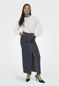 Camicia bianca a maniche lunghe con dettagli in pizzo abbinata a una gonna di jeans a vita alta con uno spacco laterale e righe verticali. Tacchi blu scuro.